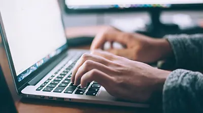 Ivans Download  Close up of hands typing on laptop keyboard.