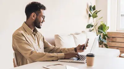 5 Industry Stats You Need to Know A man sitting at a desk while typing on a laptop with one hand and using his phone with his other hand
