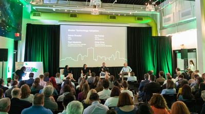 Brokers and Agencies Take a Seat at the Insurtech Table A conference with four speakers sitting on the stage while presenting to a crowd