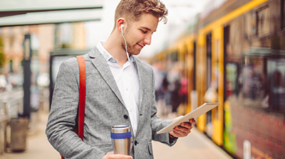 A Year of Illuminating Insights from Insurtech Godfathers & Trailblazers A man in a gray blazer wearing headphones and looking down at a tablet in one hand, while holding a travel mug in his other hand