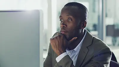 IVANS E-servicing Man dressed in business casual attire looking at computer screen with his chin resting in his hand.