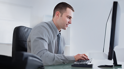 Glatfelter Insurance Group Improves Servicing Options with IVANS Man in business attire sitting at desk and typing on computer while smiling