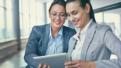 Parry & Son, Ltd. Enhances Workflow Automation and Customer Service with IVANS Two women in business attire looking down and smiling at tablet