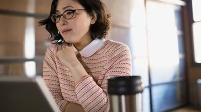 Claims Download Use Cases Woman dressed in business attire sitting and using a laptop with a portable coffee mug next to the laptop.
